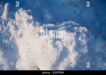 Detailed winter snow mound and drifted snow patterns, close up of bright white surface with icy sparkle and deep blue shadow background outdoors Stock Photo