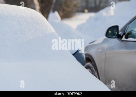 Car mirror barely visible under thick snow cover, parked vehicles in winter driveway with snowdrifts and soft sunlight, close up cold weather transpor Stock Photo