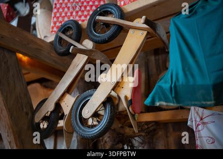 Two wooden toddler balance bikes hanging upside down in shed interior, black tires and simple frames, indoor storage of kids toys in rural outbuilding Stock Photo