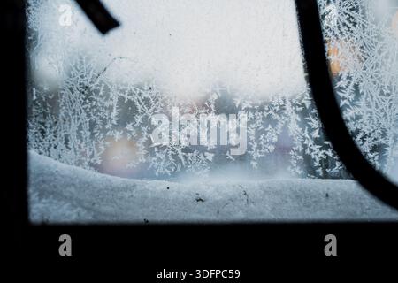 Close up of frost crystals covering window glass with snow on sill, abstract winter texture and soft blurred outdoor background framed by dark metal e Stock Photo