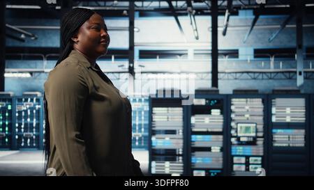 Technician in data center overseeing large scale IT gear to maintain seamless operations. IT professional walking in server hub, doing network management for increased uptime, camera A Stock Photo
