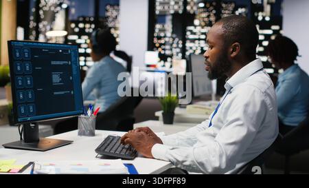 Black worker uses AI chatbot system at desktop for problem solving tasks, futuristic technology highlighting smart algorithms and machine learning. Communication and IT support. Stock Photo