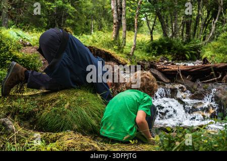Two boys crouch beside a stream in Innerdalen, playing with water while enjoying nature. The brothers explore their surroundings during a hike Stock Photo