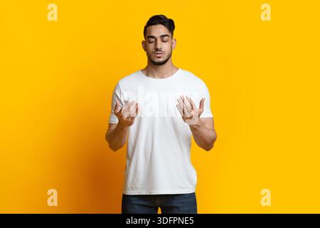 Young arab man praying for luck on yellow Stock Photo