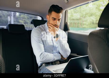 Pensive middle-eastern businessman working at car, using laptop Stock Photo