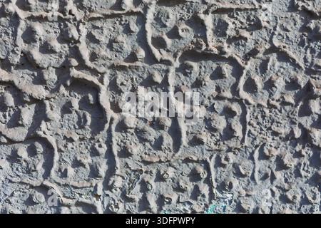 Rough gray wall reveals an intricate stucco texture with raised and indented patterns. Surface shows organic clusters and subtle wear, suggesting both Stock Photo