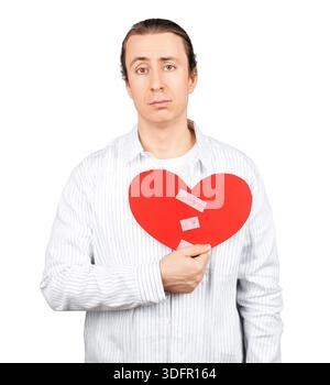 Sad man holding a broken red paper heart repaired with tape. Concept of heartbreak, reconciliation, and healing relationships isolated on white backgr Stock Photo