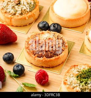 Delicious assorted tarts arranged on a wooden table, accompanied by fresh strawberries, blueberries, and raspberries, showcasing a variety of sweet tr Stock Photo