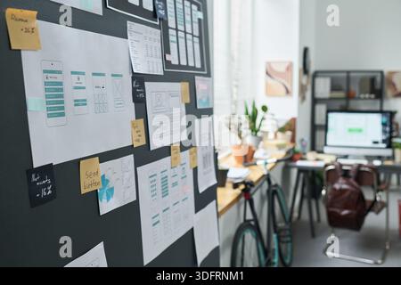 Closeup showing mobile app wireframes and user interface sketches pinned on wall in modern office, digital project planning and creative process visible with computer and bicycle in background Stock Photo