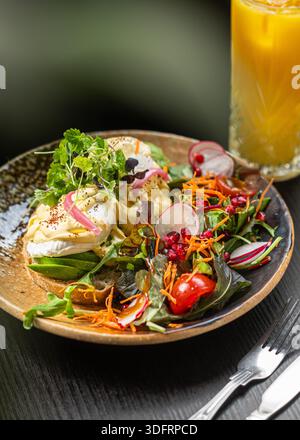 Delicious healthy breakfast featuring two poached eggs on avocado sourdough toast, garnished with microgreens and served with a vibrant side salad. Stock Photo