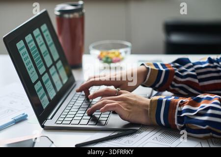 Unknown woman working on laptop, designing mobile application interface, hands typing on keyboard, digital wireframes visible on screen, office desk in background Stock Photo
