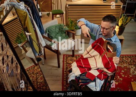 Caucasian Middle Aged Man in Wheelchair Photographing Second Hand Clothing Stock Photo