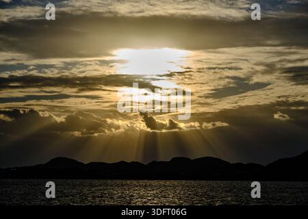 A breathtaking, high-contrast image capturing dramatic crepuscular sun rays bursting through a dense layer of dark, moody clouds. Stock Photo