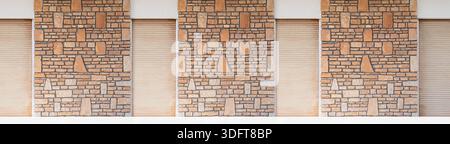 Stone wall facade featuring a pattern of natural stones and beige roller shutters Stock Photo