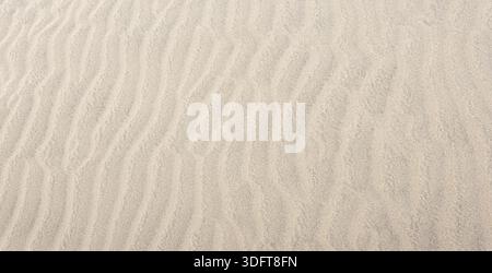 Wind creating beautiful wavy patterns in beige desert sand Stock Photo