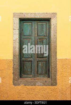 Rustic teal wooden window shutters frame a textured yellow and orange wall Stock Photo