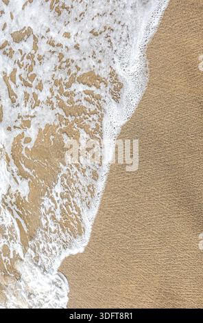 Foaming ocean water receding on textured sand, creating abstract patterns Stock Photo