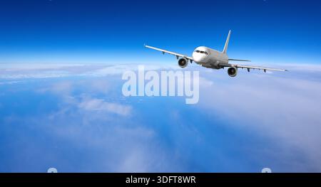 White passenger airliner flying across blue sky with clouds below, symbolizing travel and freedom Stock Photo