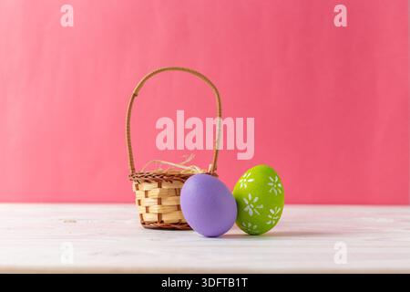 Colorful eggs and a basket are placed on a table with a pink background during springtime Stock Photo