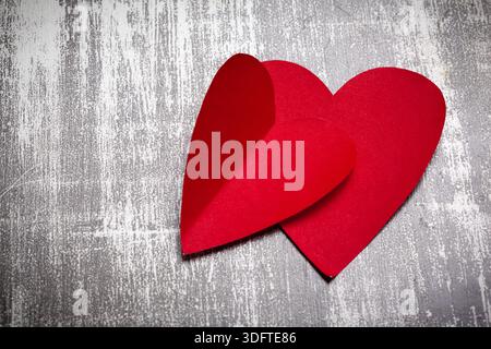 Two red paper hearts placed together on a gray textured surface Stock Photo