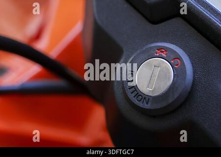 Close up motorcycle keyhole ignition switch on motorbike dashboard with black plastic and orange body showing mechanical detail and readiness for trav Stock Photo