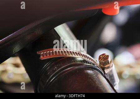 Close up shot of shiny metal hose clamp tightening black rubber tube on strong motorcycle frame showing secure and robust mechanical connection detail Stock Photo