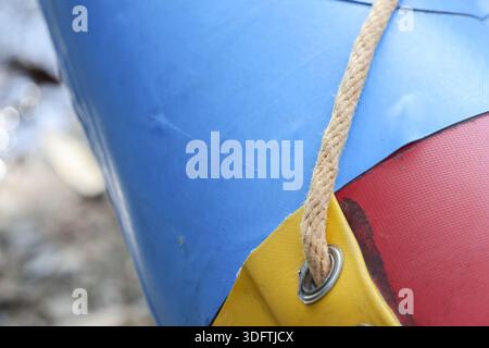 Colorful plastic tarp surface texture with strong woven rope knot tied through metal grommet shows durability of heavy material for covering outdoor c Stock Photo