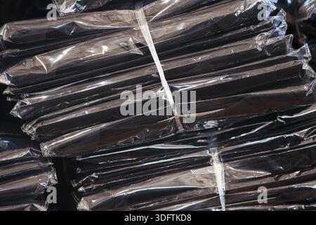 Stack of black industrial product wrapped in plastic film waiting for shipment distribution showing secure packaging and organized logistics in dark w Stock Photo