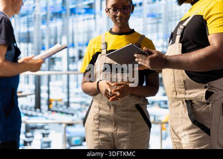 Close up of industrial workers discussing project details on metal platform in solar panel factory. Team of technicians collaborating to optimize manufacturing process using devices Stock Photo