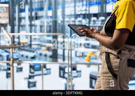 Close up of technician inspecting industrial equipment and machinery on factory floor using tablet app. Worker checking maintenance requirements for automated production units with device Stock Photo