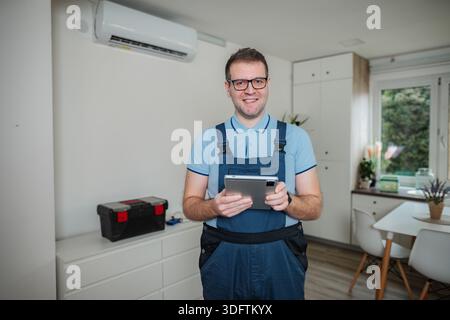 HVAC technician holding digital tablet checking apartment air conditioner Stock Photo
