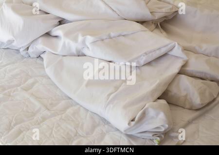 Messy white bed sheet with crumpled texture and soft pillow in morning bedroom showing cozy comfort relax and lazy feeling of unmade bedding fabric Stock Photo