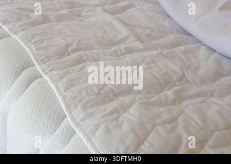 Close up view showing texture of soft white quilted mattress protector on comfortable bed with clean fabric conveying restful sleep and hygiene atmosp Stock Photo