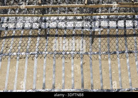 Grid pattern of steel reinforcement strip placed over chain link wire fence on dry ground showing strong and solid industrial structure for soil stabi Stock Photo