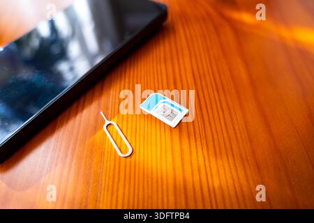 Sim Card and Eject Pin next to smartphone. nano sim card on desk, close-up Stock Photo