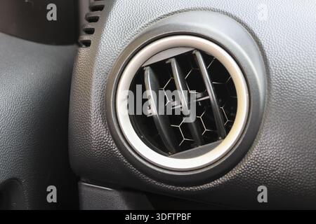 Car interior detail showing black circular air conditioner vent with silver trim ring on textured dashboard plastic panel evoking clean and modern fee Stock Photo