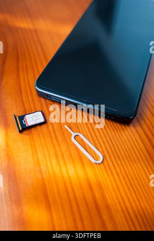 Sim Card and Eject Pin next to smartphone. nano sim card on desk, close-up Stock Photo