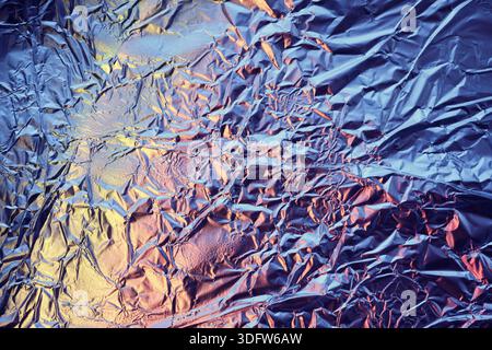 Crumpled aluminum foil surface reflecting vibrant blue and orange light Stock Photo