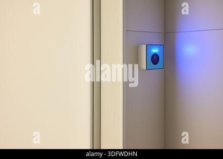 This is a modern smart touch sensor device installed on a wall, featuring a blue LED indicator Stock Photo
