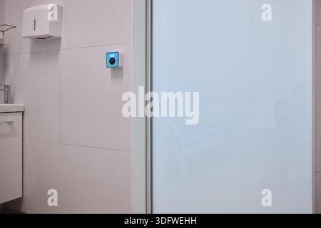 This is a modern smart touch sensor device installed on a wall, featuring a blue LED indicator Stock Photo