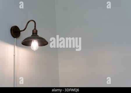 Light fixture with a bulb is hanging from a wall. The light is on and the fixture is made of metal Stock Photo