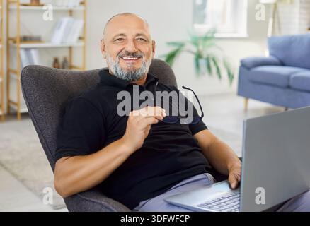 Senior man holding glasses with smile, smiling and sitting with laptop at home Stock Photo
