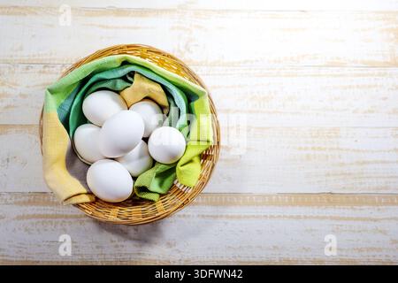 Fresh white eggs for the Easter holidays in a basket with green and yellow cloth on rustic, light-colored wood, copy space, high angle view from above Stock Photo
