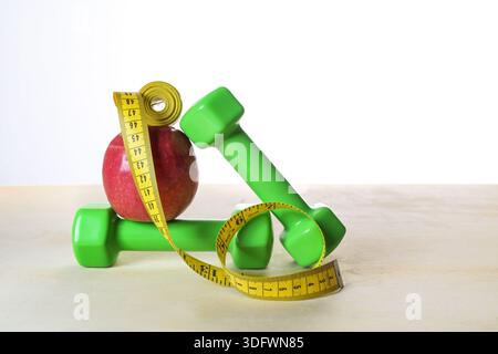 Dumbbells, apple and a, unrolled tape measure stacked in balance on light wood against a white background, healthy eating and exercise for fitness, we Stock Photo