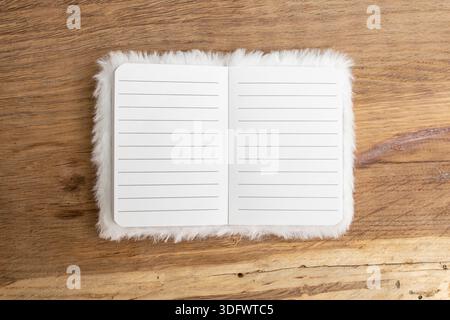 White furry cover on an empty opened notebook with lined pages on wooden desk background, abstract  backdrop Stock Photo
