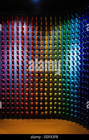 Top-down view of neatly arranged colorful sewing thread spools forming a rainbow gradient on a dark wall, creating a vibrant geometric pattern. Stock Photo
