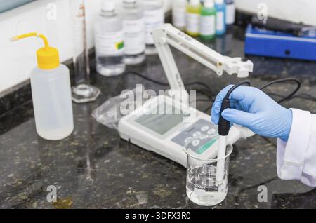 Woman hands performing pH test on pH meter electronic instrument for quality control in chemical industry Stock Photo