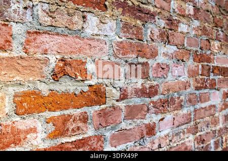 Rough red brick wall as background texture. Bricks masonry with uneven seams. View from the angle Stock Photo