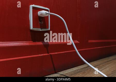 A white power cord plugs into a socket against a deep red wall. Bold color contrast and clean lines make for versatile commercial imagery. Stock Photo