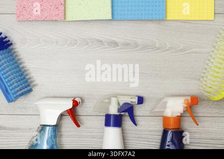 Bottles of detergent, color microfiber napkins and synthetic brushes for cleaning on gray wooden background. Set of cleaning tools and equipment Stock Photo